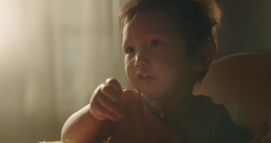 Toddler eats with their hands sitting near window indoors