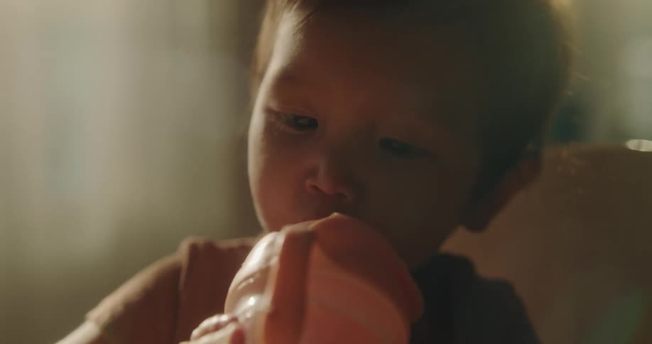 A baby plays with his water bottle as he drinks from it