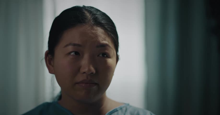 Asian woman looks sad as someone speaks to her near window
