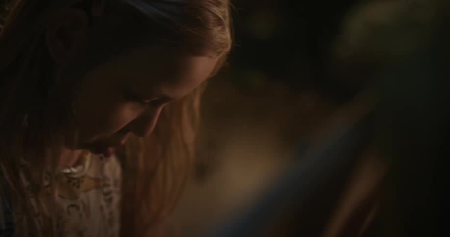 A little blonde girl in pajamas is making faces with her mouth and tongue while looking at something in front of her