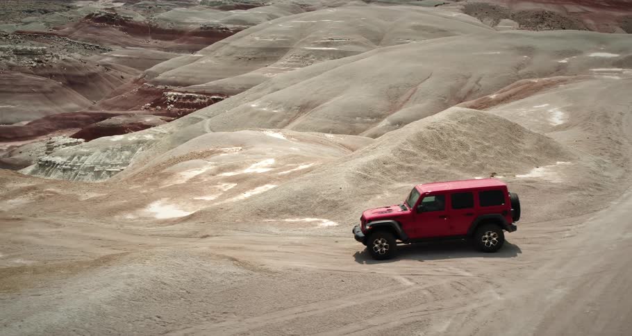 Red offroad vehicle driving on a winding dirt road through multicolored eroded hills in a desert landscape