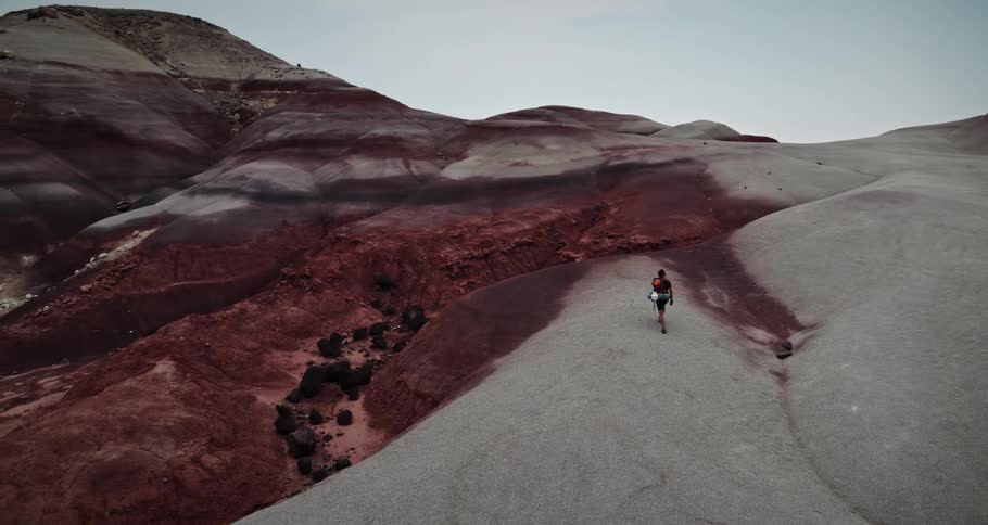A man is hiking in rock layered mountains with mountains in the distance