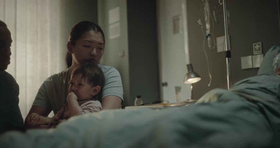 A family around a patient who is lying in a hospital bed looks at him worriedly