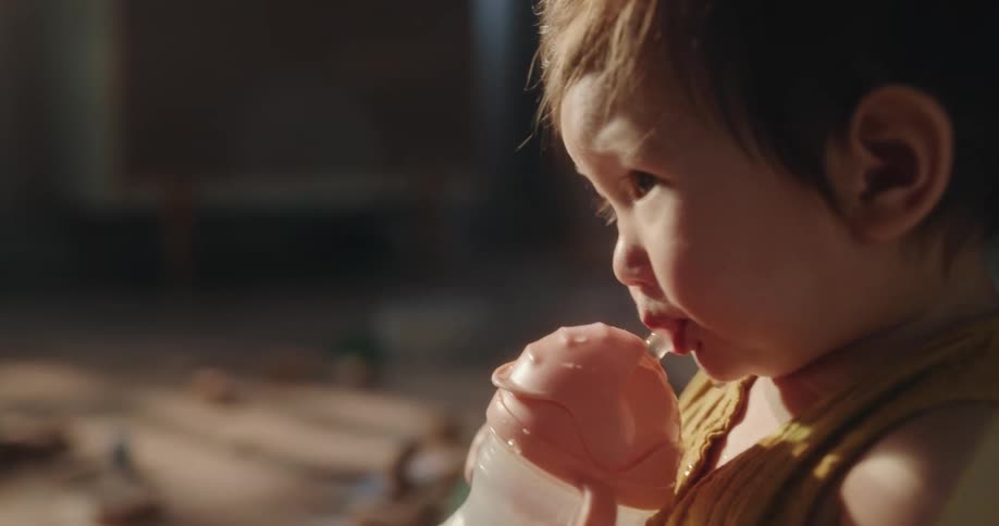 Baby drinking water from a bottle sitting on the floor surrounded by toys