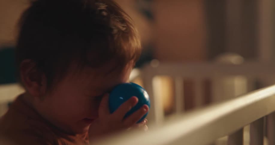 Baby yawning inside the crib and holding a small blue ball