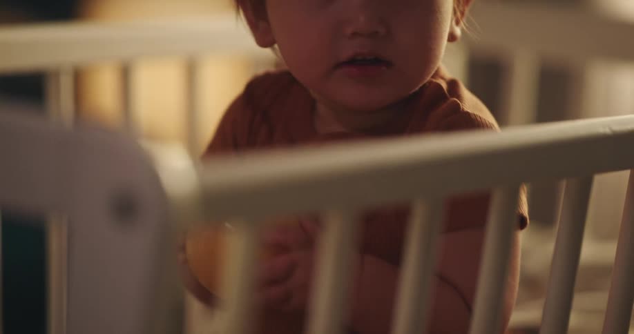 A toddler sits in her crib while clapping and holding a yellow ball