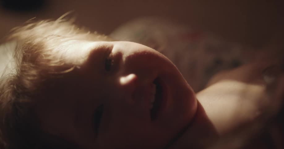 A mother playing with her baby who is lying down and smiling
