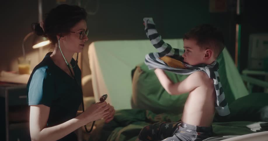 Doctor using a stethoscope to examine a young boy sitting on the hospital bed