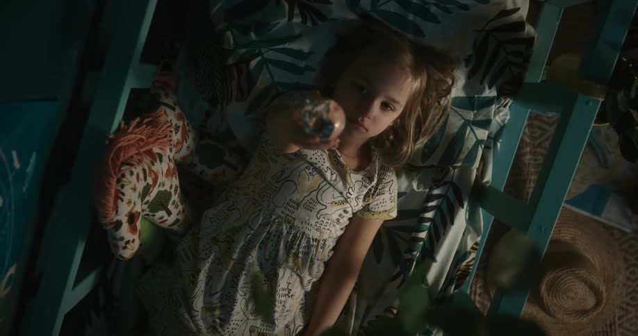 A female child holds an orb to the air while laying in a crib