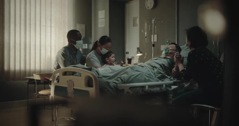 Family by the side of a man lying in a hospital bed with an oxygen mask