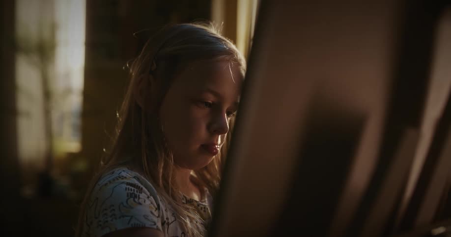 Girl paints on canvas on easel near window