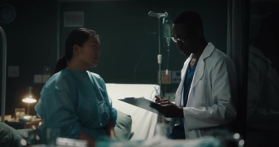 A doctor and a nurse are talking and laughing in front of a hospital bed