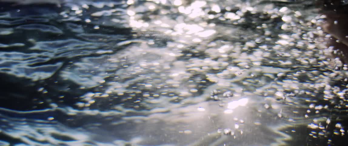 A human hand passing through the water and making a small wave