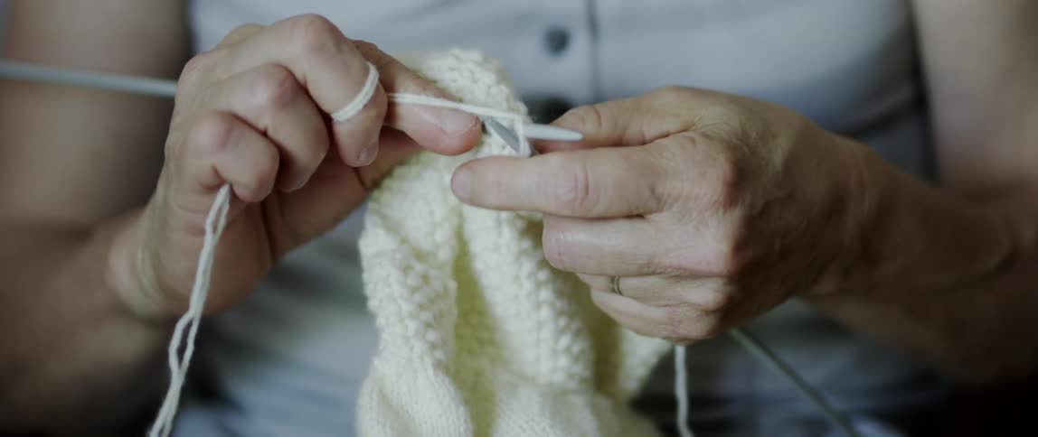 Closeup of hands knitting with white yarn