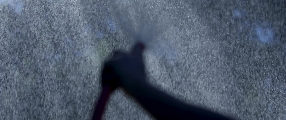 Closeup of a persons arm holding a hose upwards and releasing water