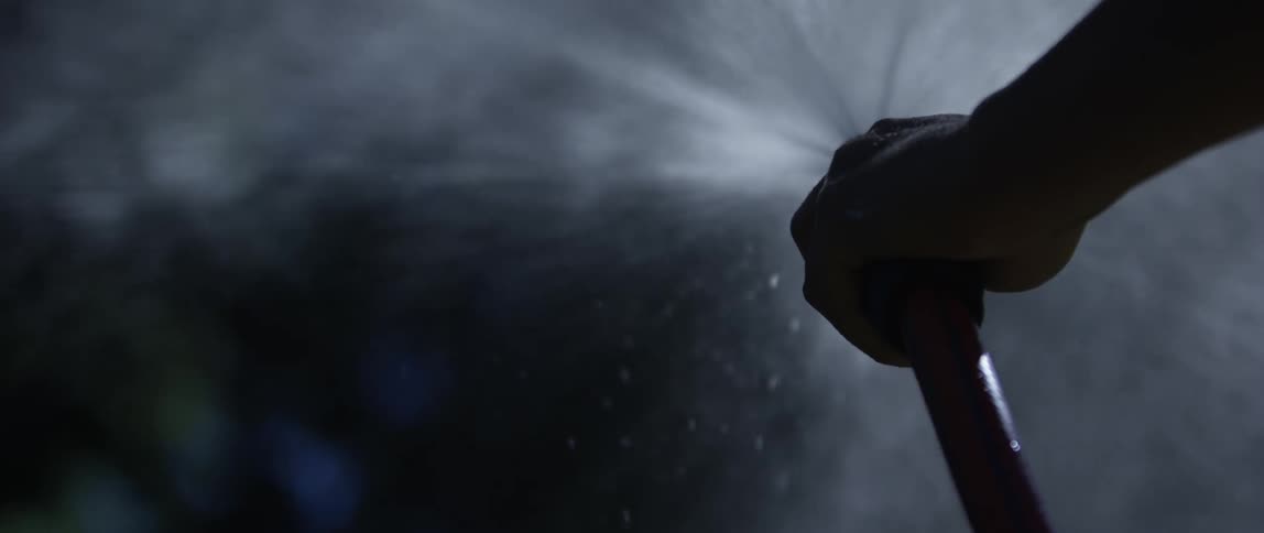 A mans arm goes back and forth as he uses a garden hose to spray water