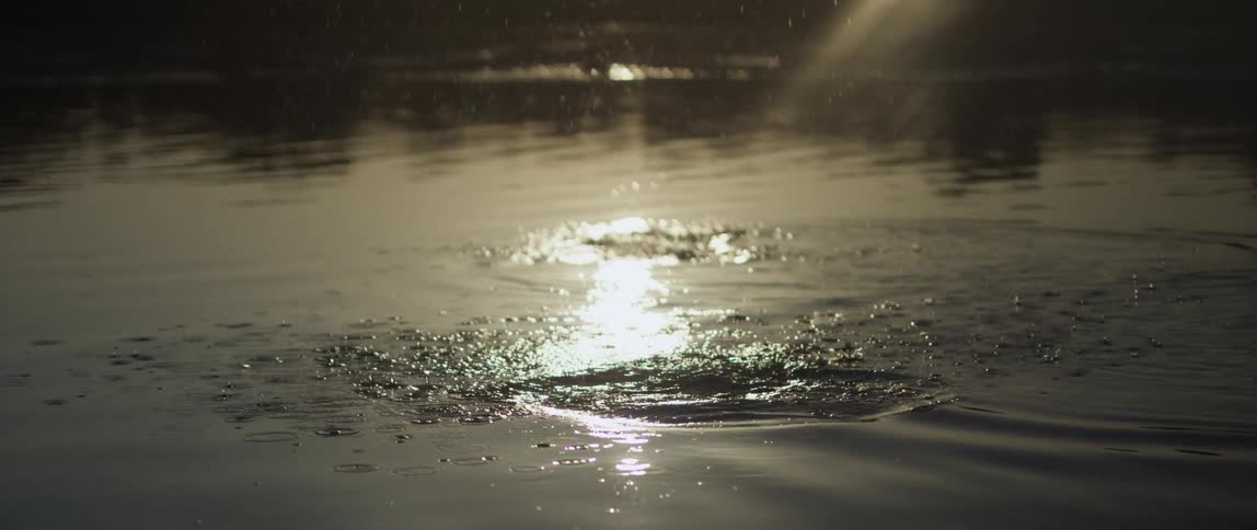 A human hand throwing a stone on the surface of a river and making a splash in the water