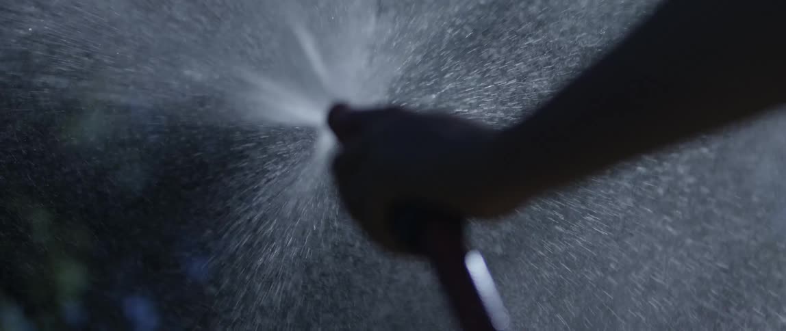 Man standing outdoors sprays water from water hose
