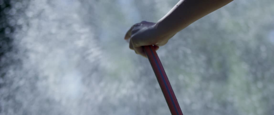 A human hand holding a hose that is throwing a lot of water forward