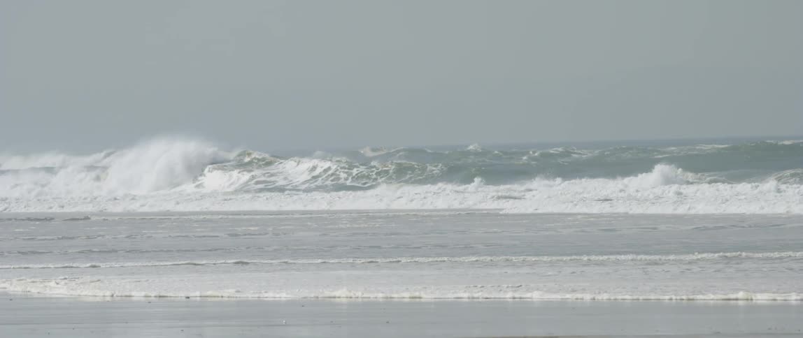 Several waves crashing on a beach with rough seas