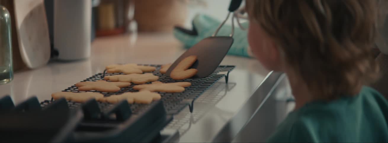 Boy watching someone removing homemade cookies and placing them in another tray