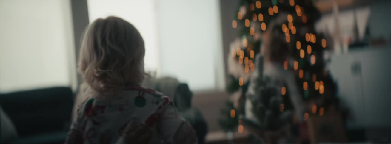 A blonde child running after another child in the living room and there is a christmas tree