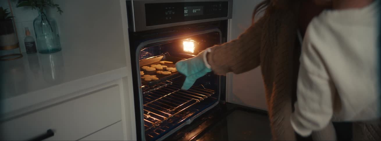 Mother carrying a boy takes a tray of freshly cooked cookies out of the oven