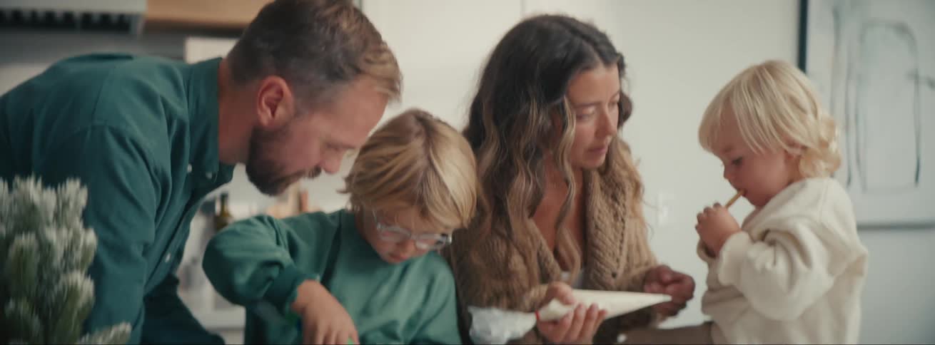 Family with two young children helping their parents prepare cookies with icing