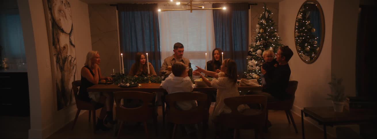 Family gathered around the dining table enjoying a christmas feast next to a beautifully adorned christmas tree
