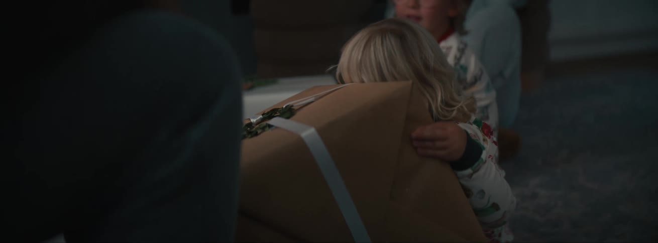 A little blonde girl in pajamas puts her head on a gift she received