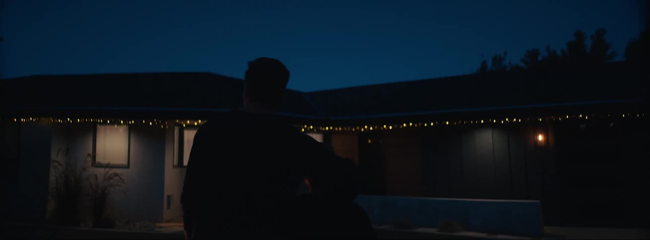 Father hugging his son in front of a house with christmas lights