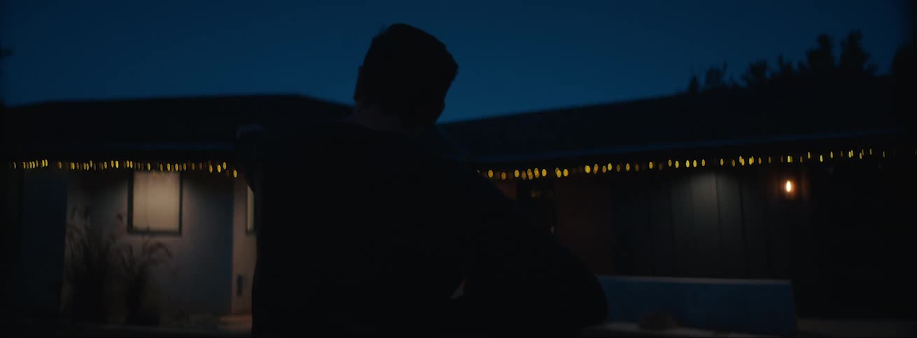 A man is looking through a screen at night outside with some yellow light blinking in a distance