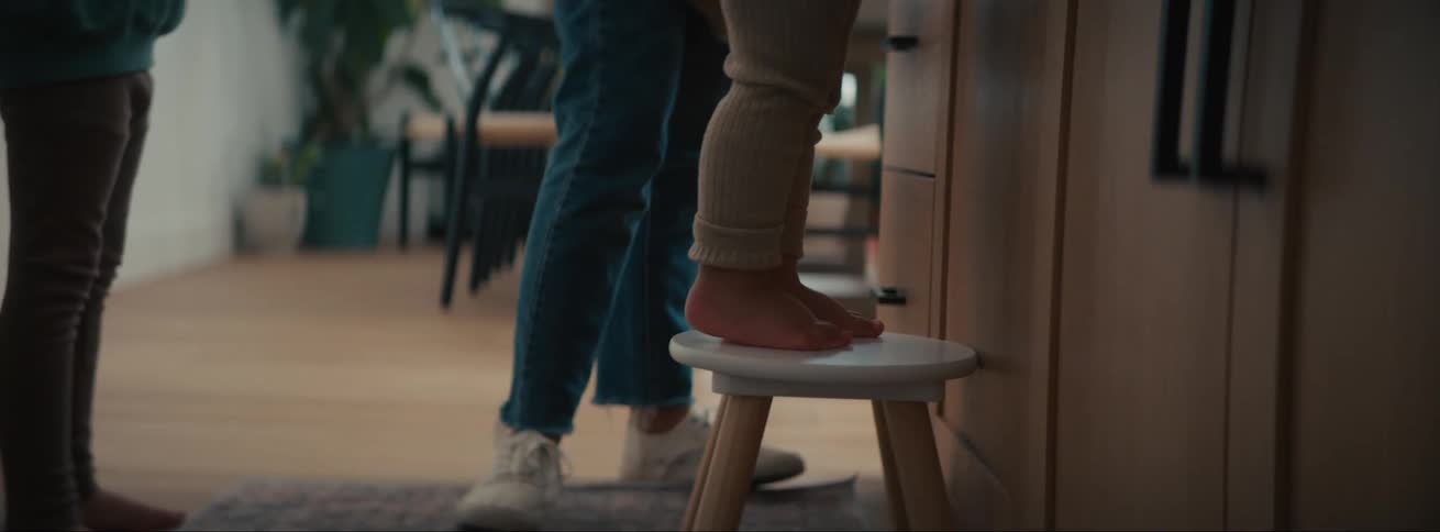 View of a family in the kitchen helping a child stand on a stool to see the countertop of a table with icing