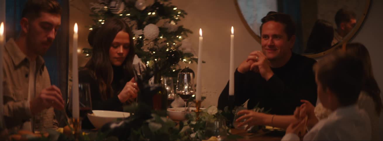 A family is eating and drinking around a candlelit table at christmas time
