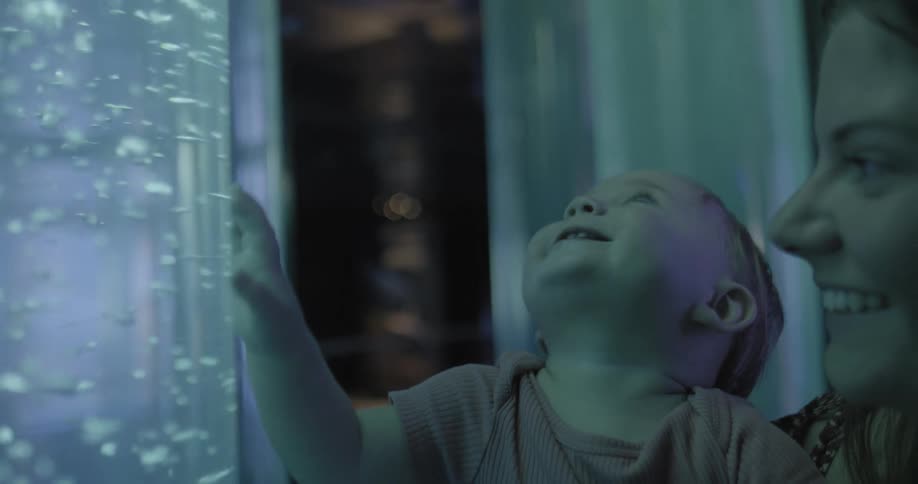 Woman holds toddler and smiles while looking at liquid with bubbles