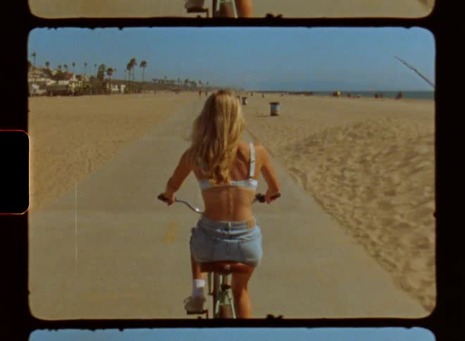 Woman riding a bicycle on a bike path in the middle of the sandy beach seen from behind