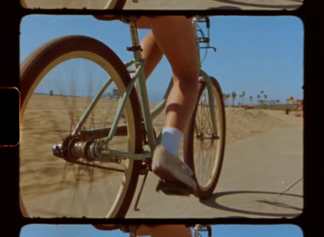Woman wearing denim shorts white socks and beige shoes rides bicycle on a road at the beach