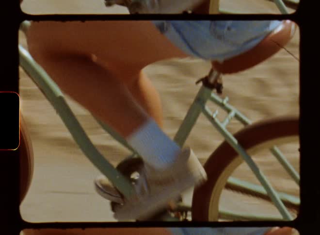 Blonde woman with sunglasses denim shorts white socks and brown shoes rides bicycle on road at the beach