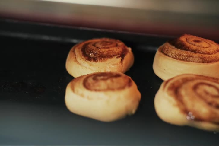 A closeup of cinnamon rolls arranged on a tray baking in the oven