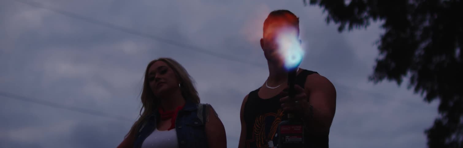 Woman stands next to man holding lit blowtorch on dim overcast day