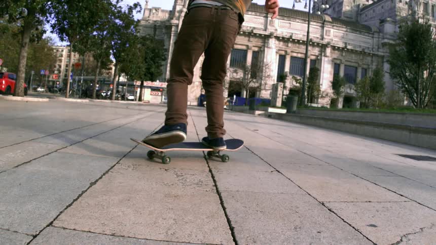 Person doing a trick with their feet up on a skateboard on a sidewalk in the middle of the city