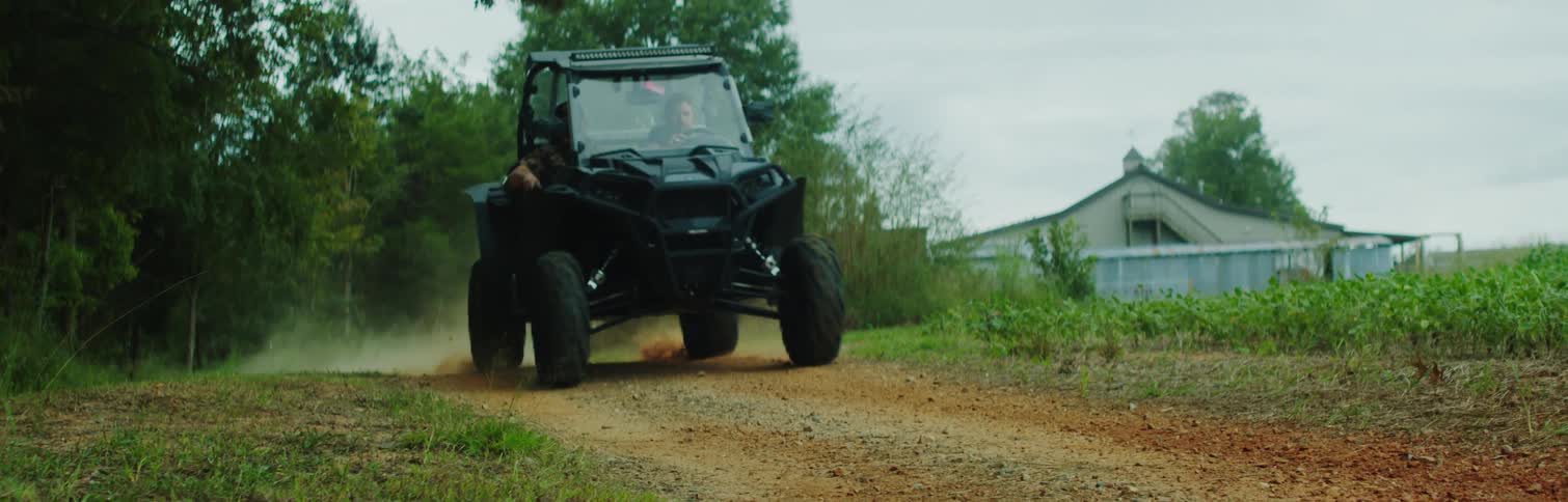 Two people in a vehicle moving on a sandy road in the evening