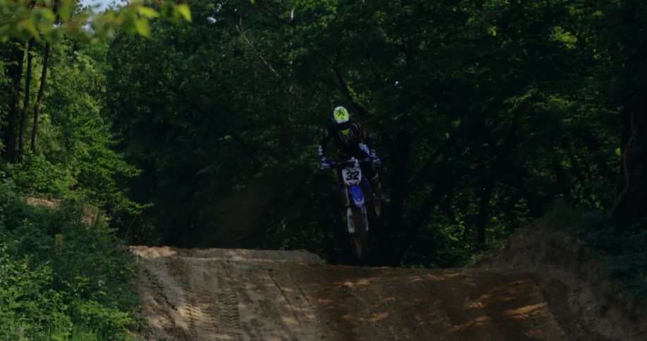 Man on a motocross bike performing stunts while jumping on a dirt track in nature