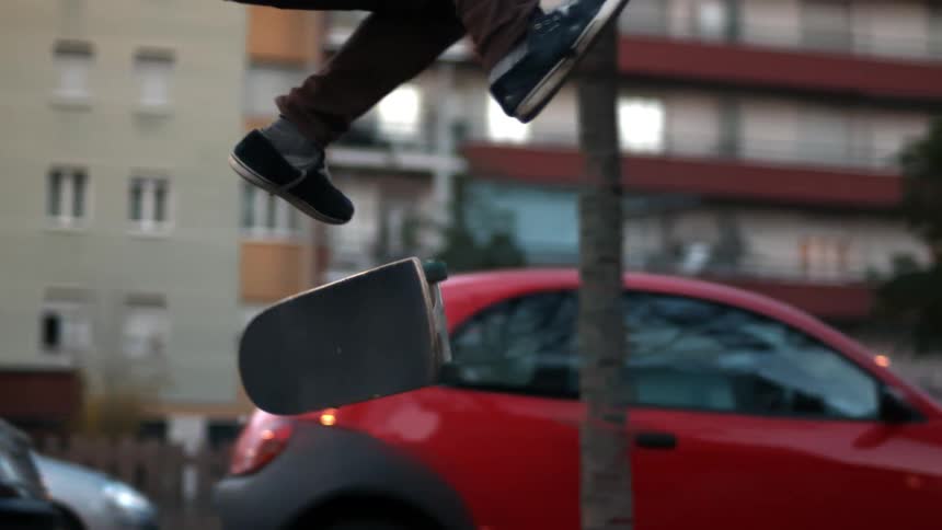 Skateboarder flips board riding near parked red car
