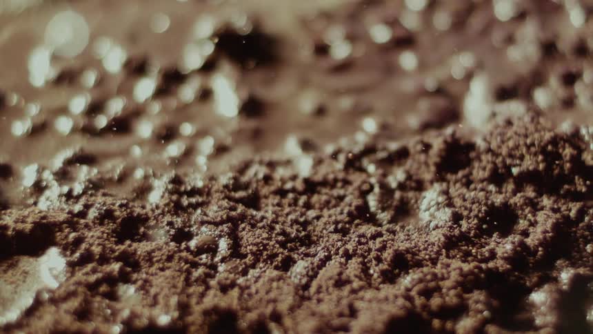Extreme closeup of water droplets falling onto brown powder