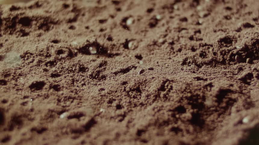 Water droplets falling in slow motion onto brown powder