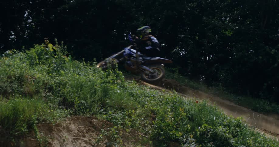 Motocross rider races up slope near trees creating dust