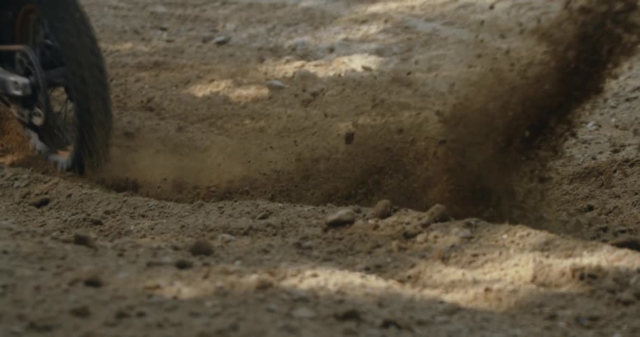 A close up of a motorbike rides through the dirt