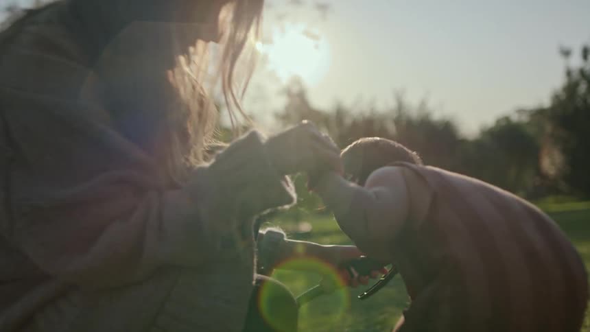 Mother holds water hose to help toddler drinkon a sunny day