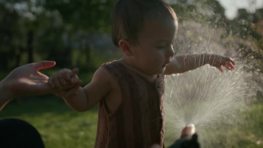 Mother sprays water onto toddler in backyard